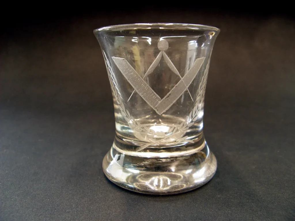Engraved masonic symbolism on glass tumbler featuring compass, square, and fronds